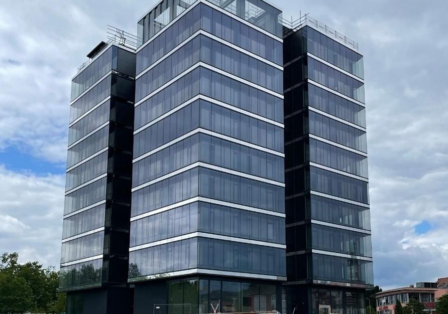 Bürohochhaus Deggendorf fast fertiggestellt, durchlaufende Glasbänder und klare Vertikalgliederung vor bewölktem Himmel.