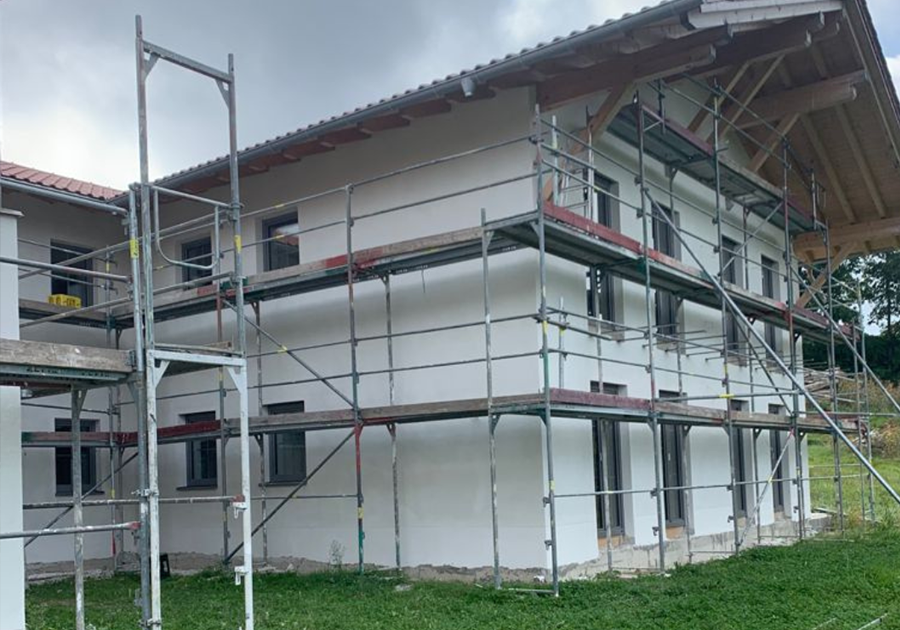 Das Bild zeigt ein zweigeschossiges Einfamilienhaus, das sich in der Bauphase befindet. Um das Gebäude ist ein Gerüst aufgestellt, und die Fassade wurde bereits mit einem Wärmedämmverbundsystem (WDVS) versehen und mit weißem Oberputz beschichtet.