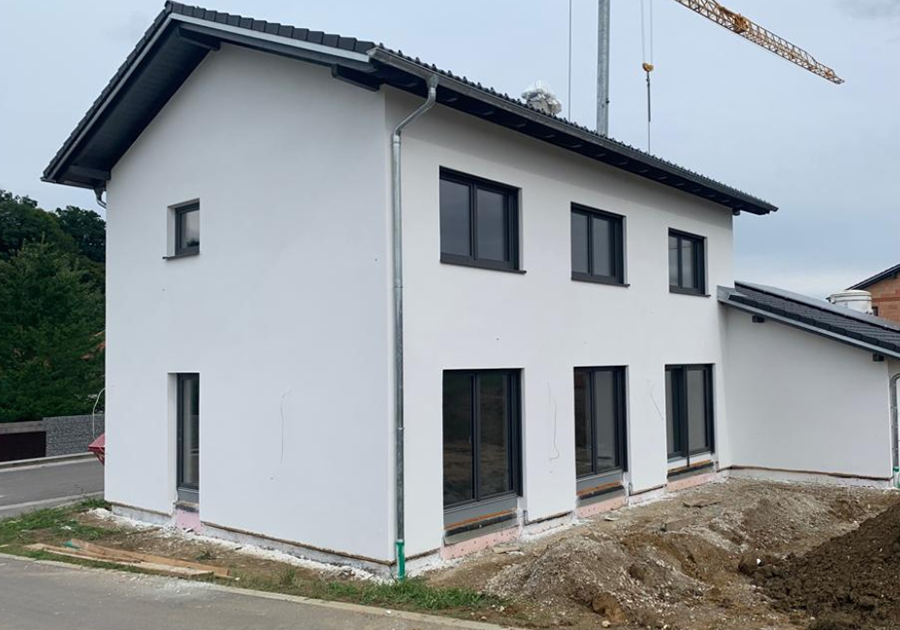 Neubau Einfamilienhaus in Mettenbach mit verputzter WDVS-Fassade, anthrazitfarbenen Fenstern und vorbereiteten Sockelanschlüssen; Außenanlagen im Aufbau.