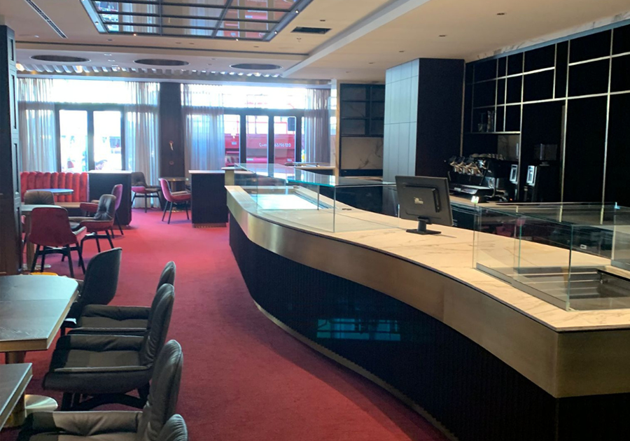 Moderne Theke mit Glasvitrine, rotem Teppich und Sitzbereichen im Kaffeehaus Deggendorf.