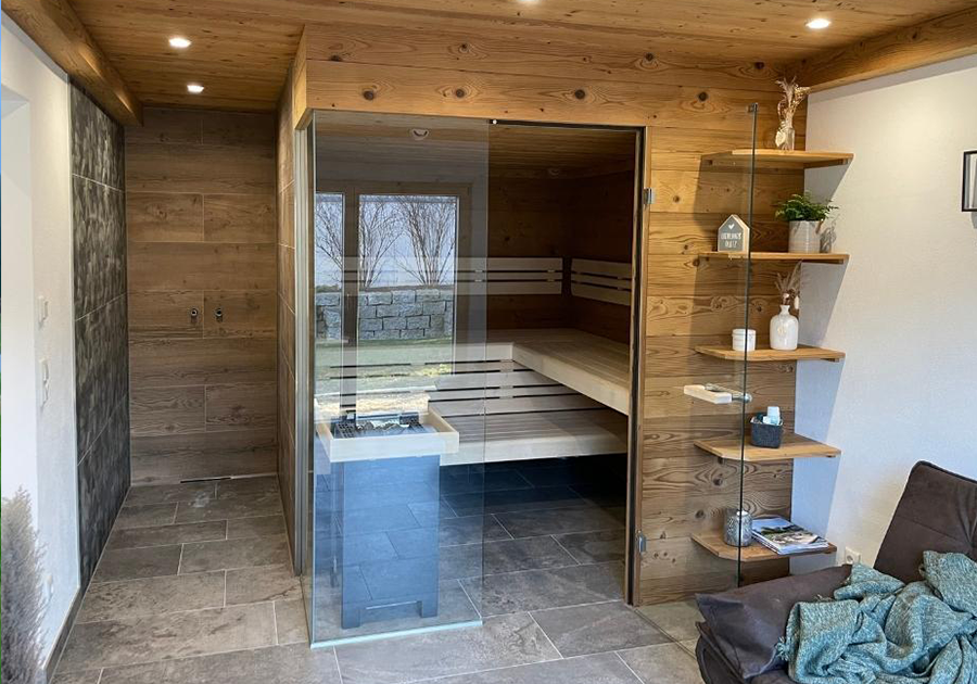 Privat-Sauna mit Holzverkleidung, Glastür, Ofen und dunklem Fliesenboden in Neuburg am Inn.